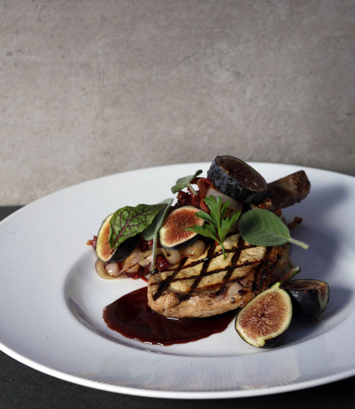 elegantly-plated grilled pork chop with chopped figs and greens